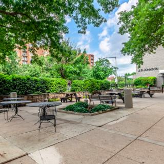 Outdoor patio area with tables and chairs surrounded by greenery in an urban setting.