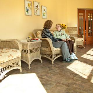 Two people sitting on wicker furniture in a sunlit room, engaged in conversation.