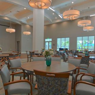 A spacious dining room with round tables and elegant chandeliers, decorated with flower arrangements.
