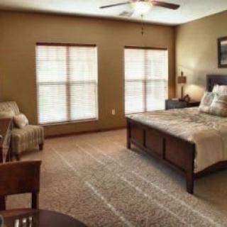 A cozy bedroom with a wooden bed, carpeted floor, and large windows.
