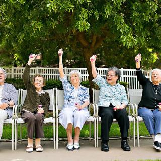 A group of elderly people sitting outdoors, each raising a fist in the air.