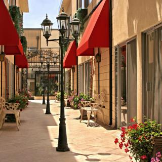 A charming alleyway lined with red awnings, street lamps, and outdoor seating on a sunny day.