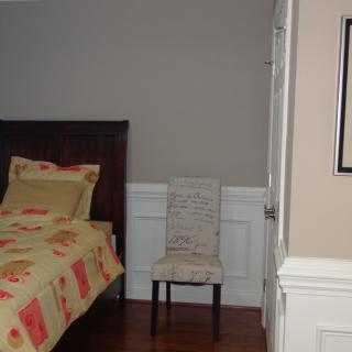 A cozy bedroom features a bed with patterned bedding, a chair, and a simple wall design.