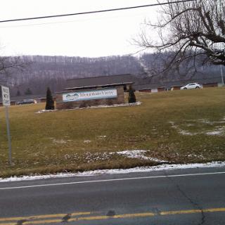 A view of a building surrounded by a grassy field and mountains in the background during winter.