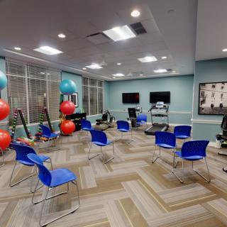 A spacious exercise room equipped with blue chairs, yoga balls, and various fitness equipment.