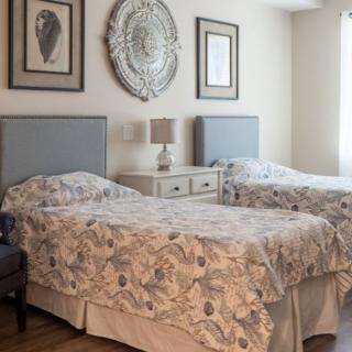 A cozy bedroom with twin beds featuring floral bedding, decorated with elegant artwork and a decorative mirror.