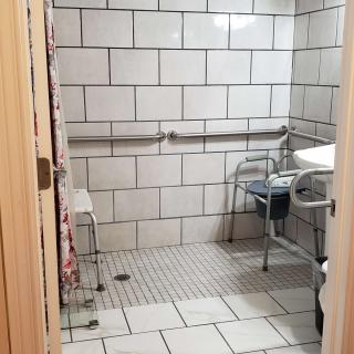 An accessible bathroom with tiled walls and floor, featuring grab bars and a shower chair for increased mobility support.