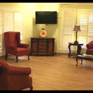 A cozy living room with red chairs, a coffee table, a television, and window shutters.