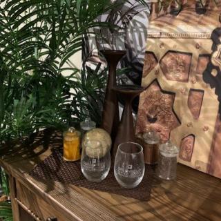 A cozy decorative setup featuring glassware, candles, and artwork on a wooden table with an indoor plant.