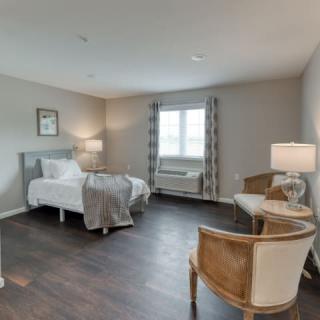 A cozy bedroom with a bed, chairs, and a window allowing natural light.