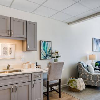A modern office space with a desk, chair, and kitchenette, accented by colorful artwork on the walls.