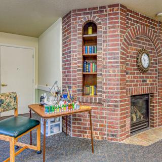 A cozy living room corner featuring a brick fireplace with an inbuilt bookshelf, a small table, and a chair.