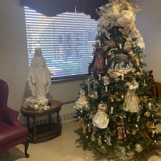A beautifully decorated Christmas tree in a cozy living room, accompanied by a statue and warm lighting.