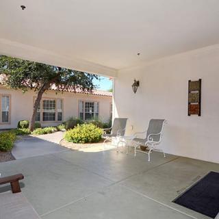 A sheltered porch area with chairs overlooking a garden and building exterior.