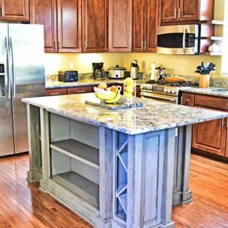 A modern kitchen with a central island featuring a granite countertop, surrounded by wooden cabinets and stainless steel appliances.