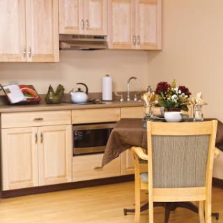 A cozy kitchen featuring light wooden cabinets, a dining table set for two, and decorative flowers.