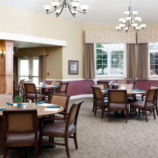 A well-lit dining room with multiple tables and chairs arranged neatly under elegant chandeliers.