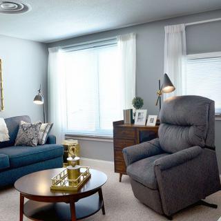 A cozy living room with a blue sofa, gray recliner, and a wooden coffee table.