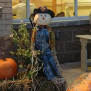 A festive outdoor display featuring a scarecrow sitting on a hay bale next to a pumpkin.