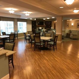 A spacious dining area with wooden floors, tables, and chairs under warm lighting.