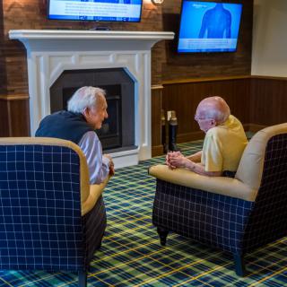 Two elderly men engaged in conversation while seated in a cozy indoor setting.