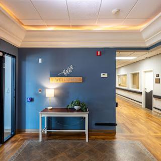 A well-lit healthcare hallway featuring a blue accent wall and a welcoming entry with a decorative table.