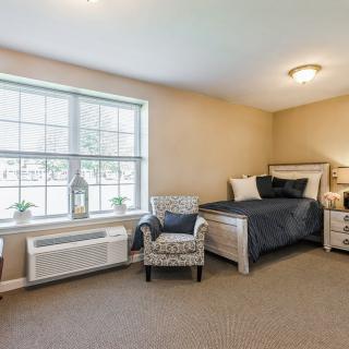 A cozy bedroom with a bed, chair, and large window allowing natural light.