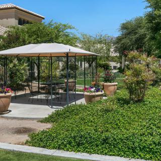 A charming gazebo surrounded by lush greenery and potted plants on a sunny day.