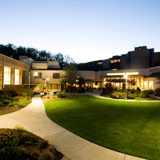 A serene view of a modern building complex during twilight, featuring well-lit pathways and green lawns.