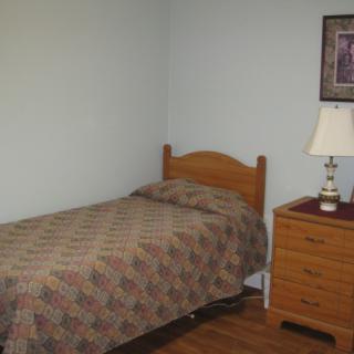 A simple bedroom with a single bed and a wooden nightstand.