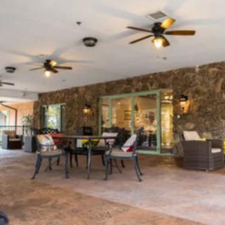 A spacious outdoor patio area with tables, chairs, and ceiling fans, set against a stone wall backdrop.