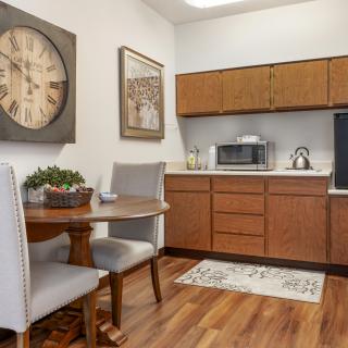 A cozy kitchen area featuring wooden cabinets, a microwave, a small dining table with chairs, and decorative elements.