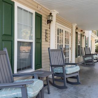 A cozy porch with several rocking chairs lined up outside a house.