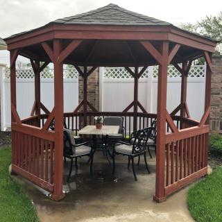 A wooden gazebo with seating and a table inside, set in an outdoor area.