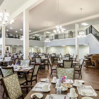 A spacious and elegantly designed dining area with multiple tables and chairs, featuring chandeliers and a mezzanine level.