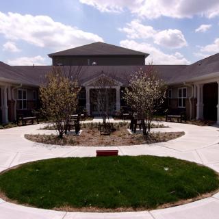 A courtyard featuring a central lawn area with young trees, surrounded by a building under a cloudy sky.