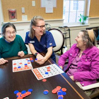 A caregiver enjoying a game of bingo with two elderly women, all smiling and engaging in a lively interaction.