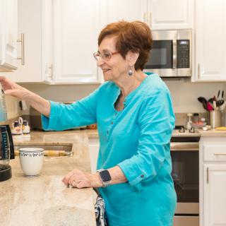 A woman in a blue shirt making coffee in a bright kitchen.