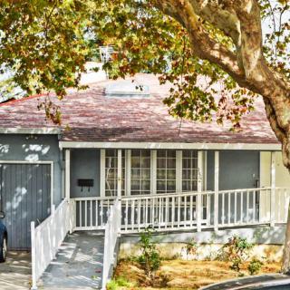 A quaint suburban house with a front porch and a tree-shaded yard.