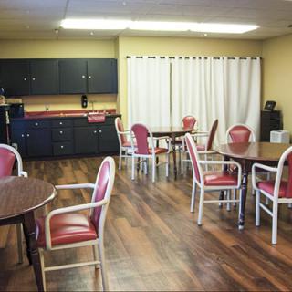 An empty dining area with several tables and chairs, featuring wooden flooring and cabinets.
