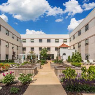A courtyard garden surrounded by a large, white building under a blue sky with clouds.