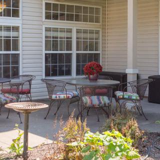 A cozy patio with a table and chairs, adorned with red flowers, set against a background of large windows.