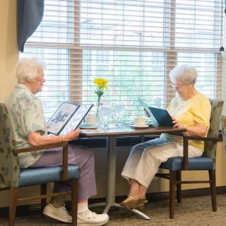 Two elderly women sitting at a table in a restaurant, looking at menus.