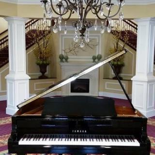 A grand piano in a luxurious interior with a chandelier and staircase.