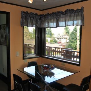 A cozy dining area with a glass table and chairs, featuring large windows that offer an outdoor view.