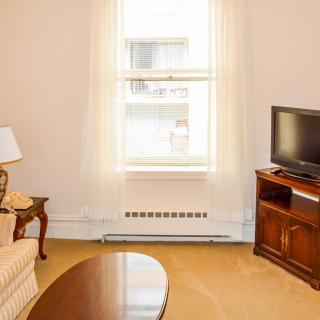 A cozy living room with a sofa, table, lamp, and a television near a bright window.