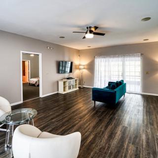 A spacious and modern living room with wood flooring, featuring a teal sofa and minimalistic decor.