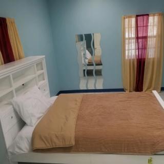 A minimalist bedroom featuring a neatly made bed with soft brown bedding, light blue walls, and colorful curtains.