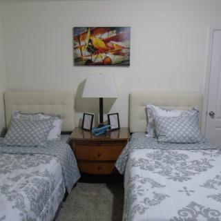 A cozy bedroom with twin beds and a nightstand accompanied by a lamp and decorative artwork.