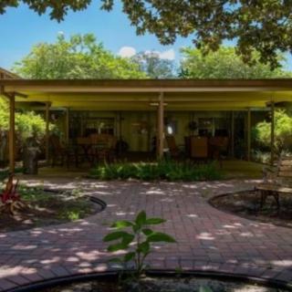 A mid-century modern house surrounded by a lush garden and patio area.